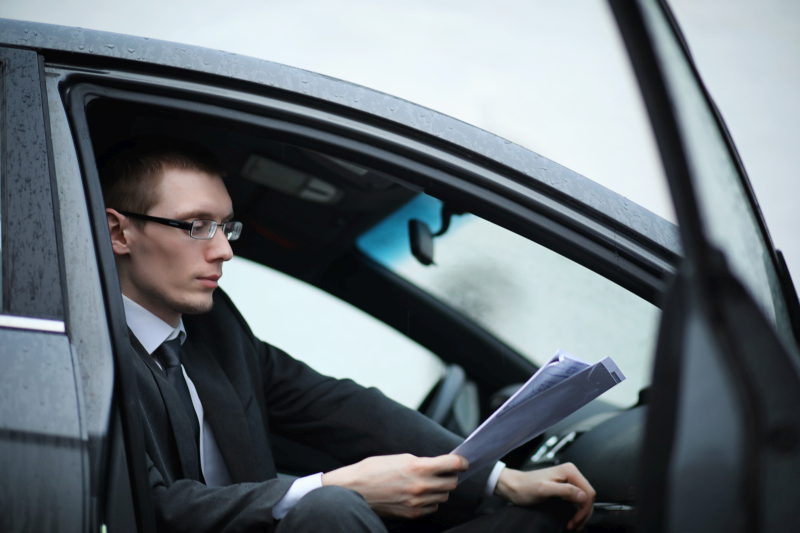muž sediaci v aute s otvorenými dvermi drží papiere